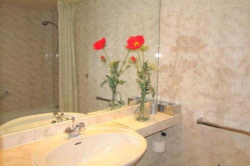 ein Badezimmer mit einem Waschbecken und zwei roten Blumen in der Unterkunft Apartmentvermittlung Mehr als Meer - Objekt 4 in Timmendorfer Strand
