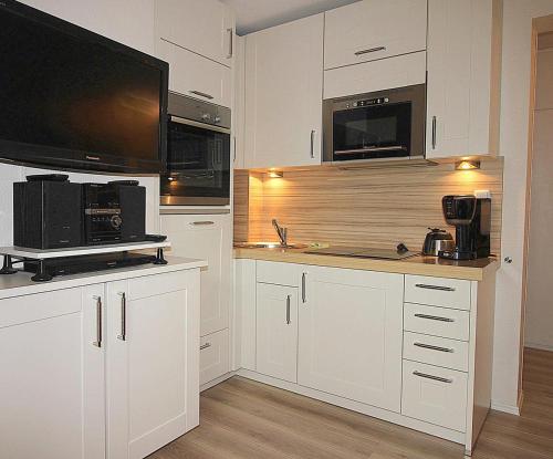 a kitchen with white cabinets and a flat screen tv at Apartmentvermittlung Mehr als Meer - Objekt 48 in Niendorf