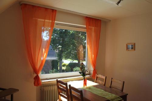 a dining room table and a window with orange curtains at NEU! Ferienwohnung im Leegmoor in Aurich