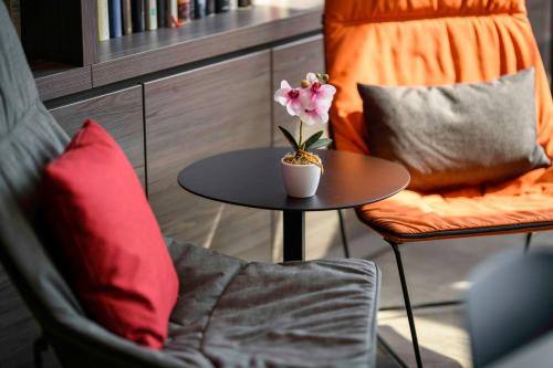 a table with a vase with a flower on it next to a chair at Campanile Berlin Brandenburg Airport in Schönefeld