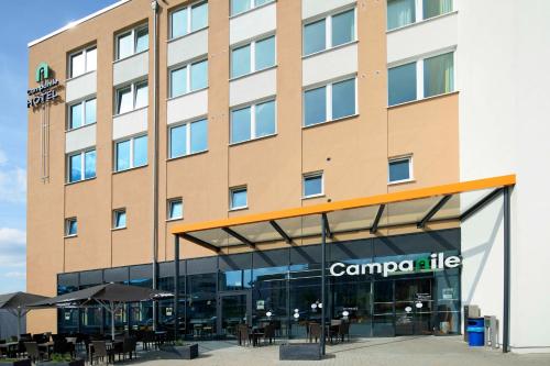 a hotel building with tables and umbrellas in front of it at Campanile Berlin Brandenburg Airport in Schönefeld