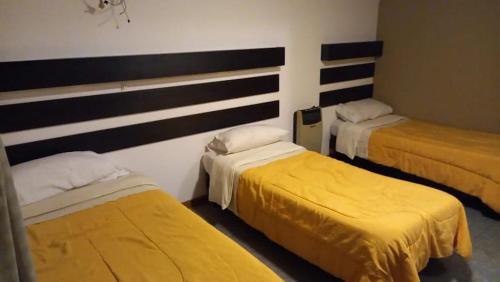 a room with three beds with yellow sheets at Hostel Los Andes in Guaymallen