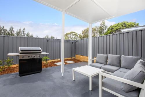 a patio with a couch and an umbrella and a grill at East Side Sands - Pet Friendly - 5 Mins Walk to Beach in Culburra Beach
