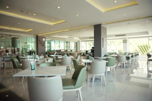 um restaurante com mesas brancas e cadeiras verdes em Tamarind Garden Hotel - SHA Plus Certified em Rayong