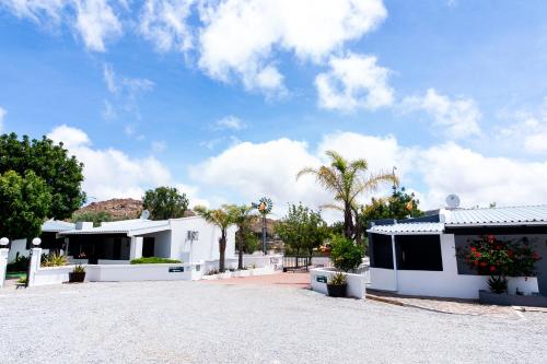 a white building with trees and palm trees at Kleinplasie Guesthouse in Springbok