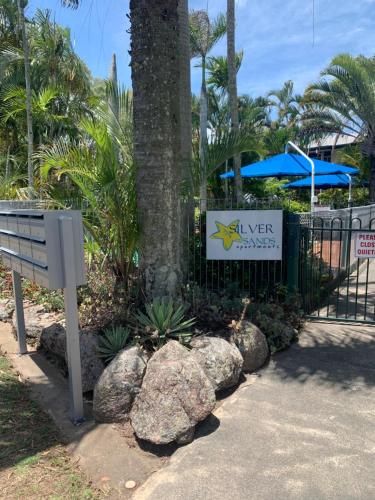 a sign next to a tree with rocks next to a fence at The Bay Beach Shack, Hervey Bay in Hervey Bay