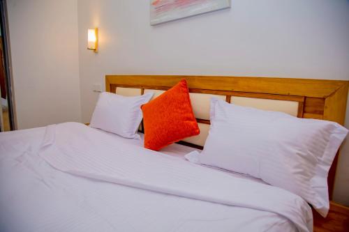uma cama com lençóis brancos e almofadas laranja em The View Apartments Kigali em Kigali