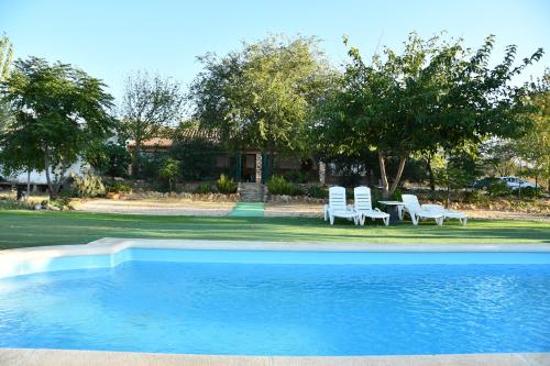 a swimming pool with two white chairs and a house at Casa Rural La Loma in Cabeza del Buey