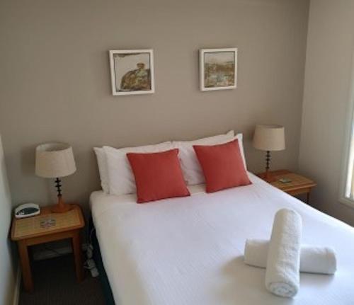 1 dormitorio con 1 cama blanca grande con almohadas rojas en Captain's Quarters Bermagui, en Bermagui