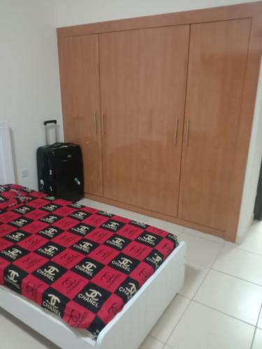 a bed with a red and black blanket and a cabinet at SHAFA Holiday Homes in Dubai
