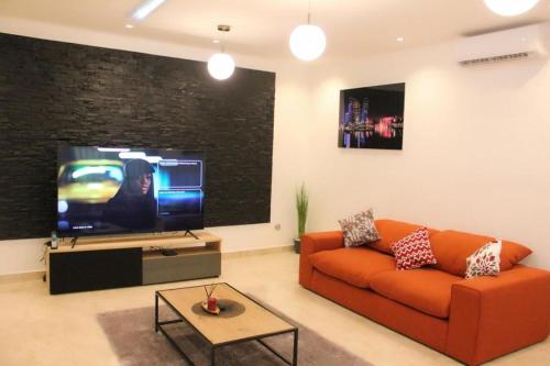 sala de estar con sofá naranja y TV de pantalla plana en RESIDENCE MH SERVICES Cotonou, en Cotonou