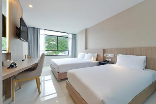 a hotel room with two beds and a desk at Grace Patong Hotel in Patong Beach