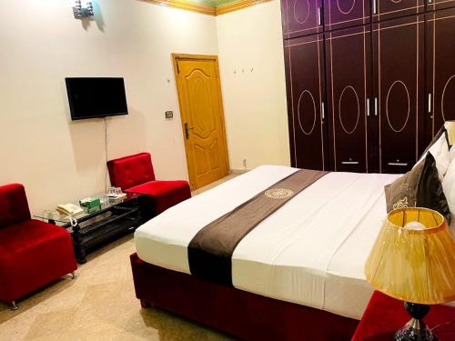 a bedroom with a bed and two chairs and a television at Infinity Hotel in Lahore