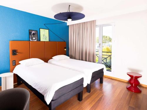 2 camas en una habitación con una pared azul en ibis Valenciennes, en Valenciennes