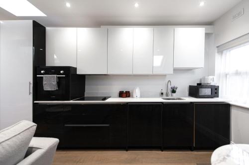a kitchen with white cabinets and a black refrigerator at Ealing Residency in London