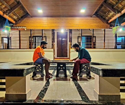 two men sitting at a table in a room at Caffeine Villa in Kaniyāmbetta