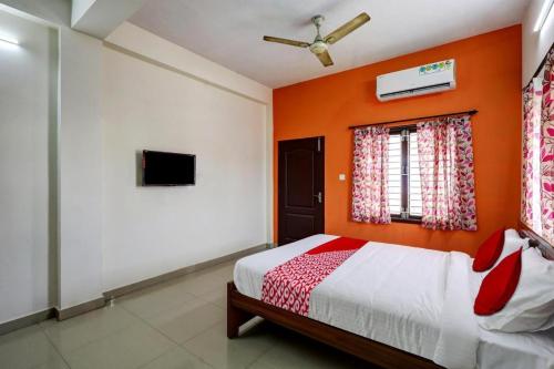 a bedroom with an orange wall with a bed and a window at Simsan Inn in Chennai