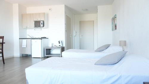 two beds in a white room with a kitchen at Zenao Appart'Hotel in Yzeure