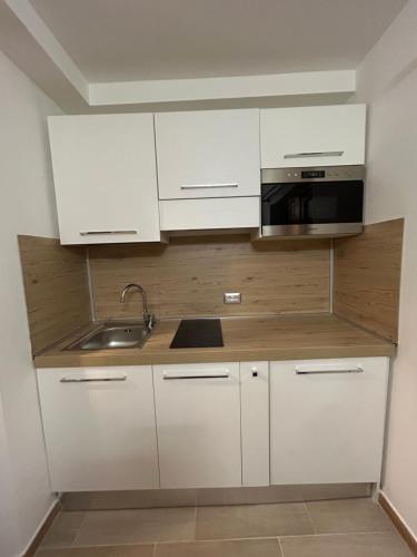 une cuisine avec des armoires blanches, un évier et un micro-ondes dans l'établissement Casa Genziana - nuovo bilocale in centro a Sestriere, à Sestrières