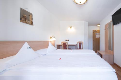 a bedroom with a large white bed and a table at Hotel Zirmes in Moena