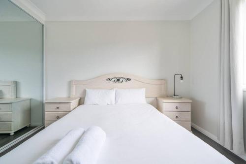 a white bedroom with a large white bed and a mirror at Large Family Home with plenty of amenities in Campbelltown