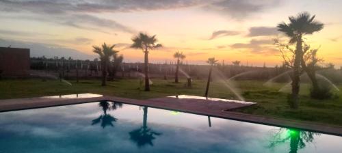 una piscina con palmeras y una puesta de sol en Igrane House, en Marrakech