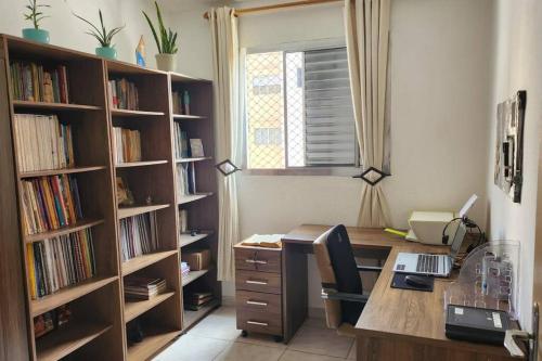 ein Büro mit einem Schreibtisch mit einem Computer und Bücherregalen in der Unterkunft Sinta-se em Casa Longe de Casa in Taboão da Serra