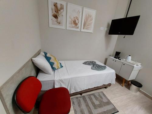 Habitación pequeña con 1 cama y 2 sillas rojas en Kitnets bem localizada, próx ao autódromo! en Londrina