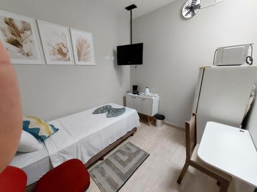 Cette petite chambre blanche comprend un lit et une chaise. dans l'établissement Kitnets bem localizada, próx ao autódromo!, à Londrina