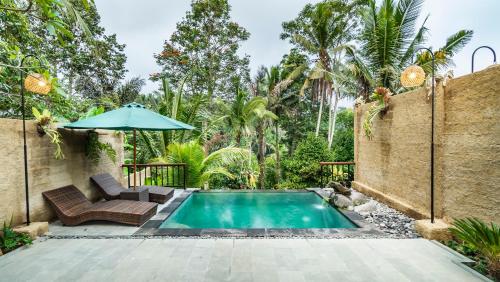 a swimming pool with a patio furniture and an umbrella at Uma Kakul Villas in Tegalalang