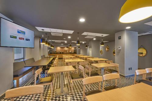 a cafeteria with tables and chairs and a large screen at City Express Plus by Marriott Ciudad de México Periférico Sur Tlalpan in Mexico City