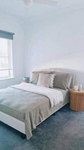 Un dormitorio blanco con una cama con almohadas y una ventana en Foxy's Cottage, en Point Cook