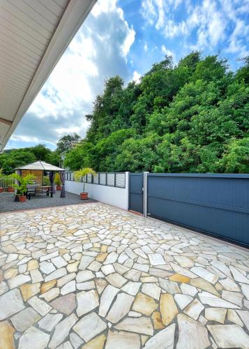 a stone patio with a fence and trees at Villa Sweet Caraïbes, vue mer, jacuzzi in Les Trois-Îlets