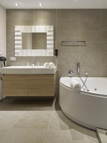 ein Badezimmer mit Badewanne, Waschbecken und Spiegel in der Unterkunft Romantik Parkhotel het Gulpdal in Slenaken