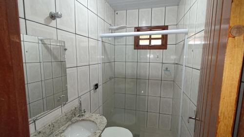 ein weiß gefliestes Bad mit einem WC und einer Dusche in der Unterkunft Pousada do Didi Chapada dos Guimaraes. in Chapada dos Guimarães