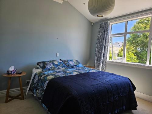 a bedroom with a bed with a blue comforter and a window at Aspiring Villa Apartment in Christchurch