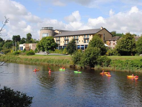 a group of people kayaking on a river in front of a building at The Riverside Park Hotel in Enniscorthy