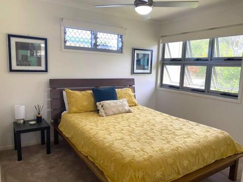 1 dormitorio con 1 cama con edredón amarillo y 2 ventanas en Anthea's on Dugong, en Tin Can Bay