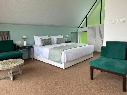 a bedroom with a bed and two green chairs at Hummingbird St.Clare Villas in Dimbula
