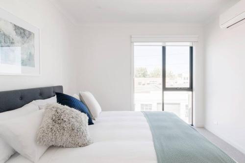 a white bedroom with a large bed with blue pillows at Perfect Port Melbourne Townhouse in Melbourne