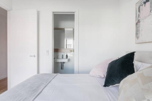 a white bedroom with a large bed with black pillows at Perfect Port Melbourne Townhouse in Melbourne