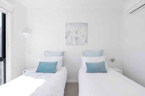 two beds in a white room with blue pillows at Perfect Port Melbourne Townhouse in Melbourne