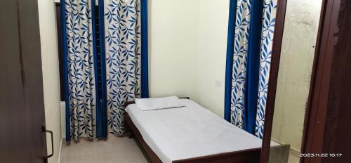 Cama pequeña en habitación con cortinas azules y blancas en Viva la Veda, en Karunāgapalli