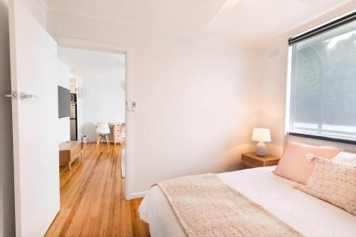 a white bedroom with a bed and a large window at Orton Waves- Beach Life Awaits in Ocean Grove