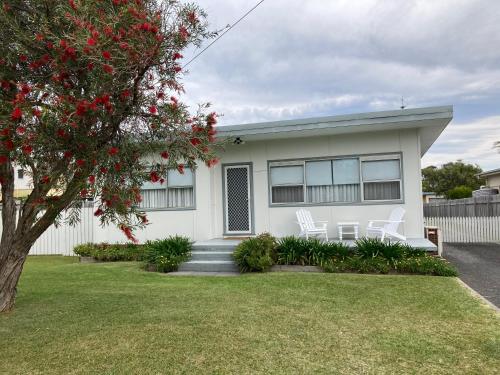 a white house with two white chairs in a yard at SummerBreeze - just a 60 second stroll to the beach in Culburra Beach