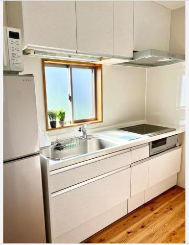a white kitchen with a sink and a window at ハルク キャビン in Nakijin