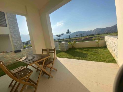 a wooden table and chairs on a patio with a view of the ocean at Lovely studio apartment inside Jebel Sifah resort in As Sīfah