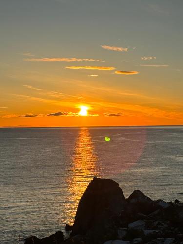 a sunset over the ocean with a rock in the foreground at Buodden Rorbuer - Fisherman Cabins Sørvågen in Sørvågen