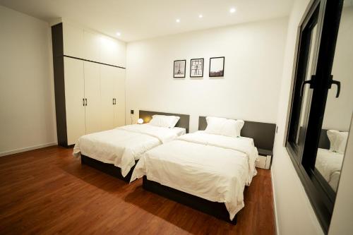 um quarto com 2 camas com lençóis brancos e pisos de madeira em Heddin Homestay em Ben Tre
