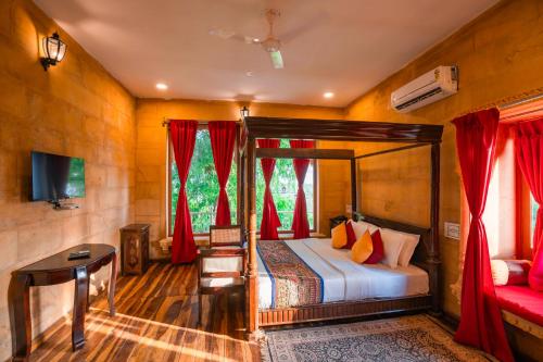 a bedroom with a bed and a desk and red curtains at Hotel Helsinki House in Jaisalmer